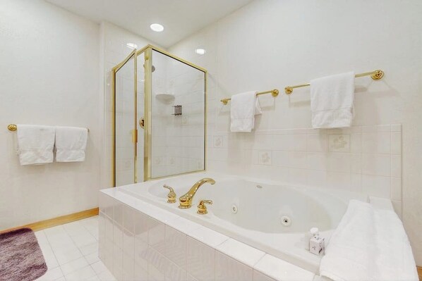 A bathroom with a large bathtub, a glass-enclosed shower, and multiple white towels on towel racks.