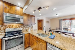 A kitchen with wooden cabinets, a granite countertop, stainless steel appliances, and a dining area with a window. - Riverfront, ground-floor condo with fireplace & fishing access - near Riverwalk (Edwards)