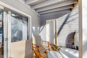 A covered porch with two wicker chairs, a small round table, and a door leading to the interior. - Riverfront, ground-floor condo with fireplace & fishing access - near Riverwalk (Edwards)