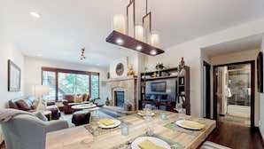 A spacious living room with a fireplace, a dining area with a long wooden table, and a comfortable seating arrangement. - Ski in/out mountain getaway with pool, hot tub, & balcony - steps to the slopes (Edwards)