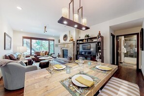Ein geräumiges Wohnzimmer mit Kamin, eine Essecke mit einem langen Holztisch und eine gemütliche Sitzecke.