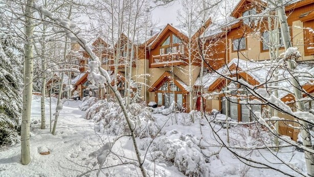 A snow-covered lodge with multiple wooden buildings, a clear path, and leafless trees. - Ski in/out mountain getaway with pool, hot tub, & balcony - steps to the slopes (Edwards)
