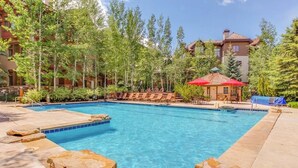 A rectangular pool with clear blue water, surrounded by stone steps and lounge chairs. - Ski in/out mountain getaway with pool, hot tub, & balcony - steps to the slopes (Edwards)