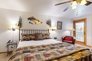 A bedroom with a large bed, a ceiling fan, two bedside lamps, a red chair, and a window with blinds. - Ski-in/out Lionshead Village studio w/ fast WiFi & shared pool/hot tubs/laundry (Vail)