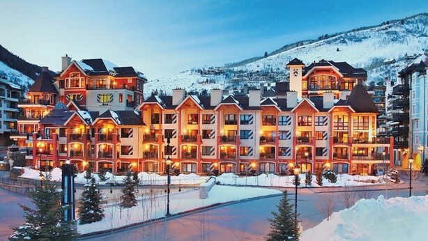 Ein mehrstöckiges Hotel mit einer symmetrischen Fassade, Balkonen und einer Skipiste im Hintergrund.