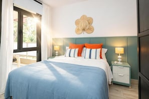 Un dormitorio con una cama, dos mesitas de noche, un adorno en la pared y una ventana con cortinas.