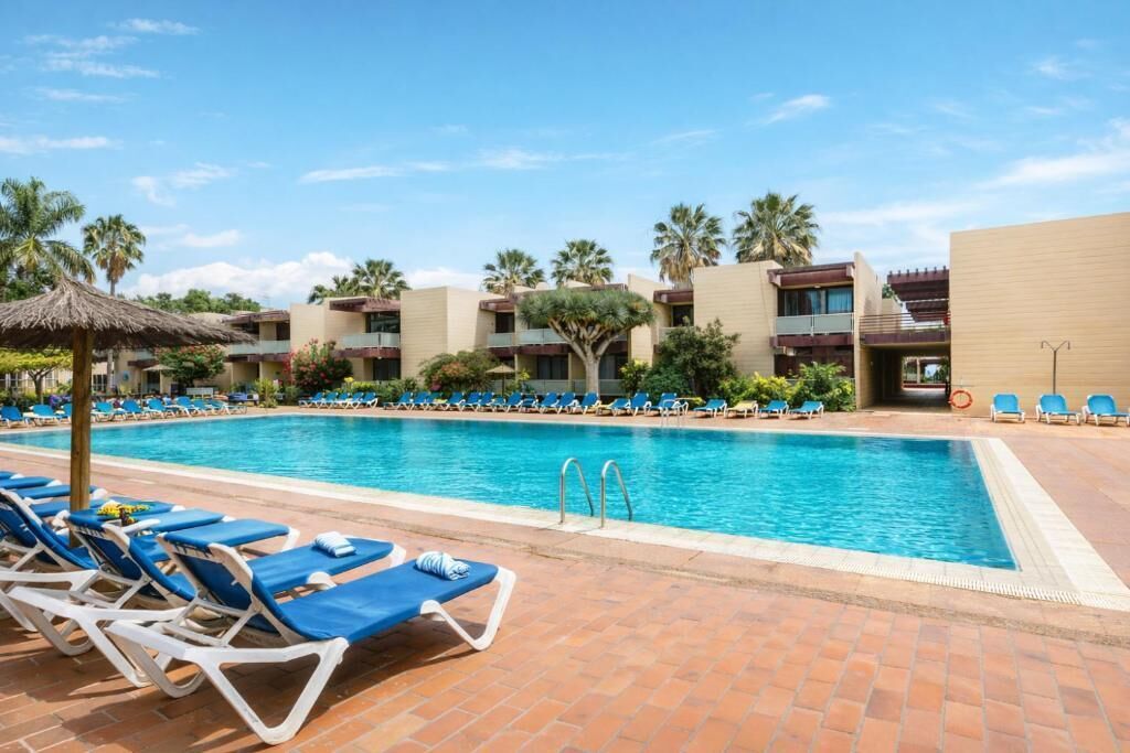 Une piscine avec des chaises longues, des palmiers et un bâtiment doté de balcons.