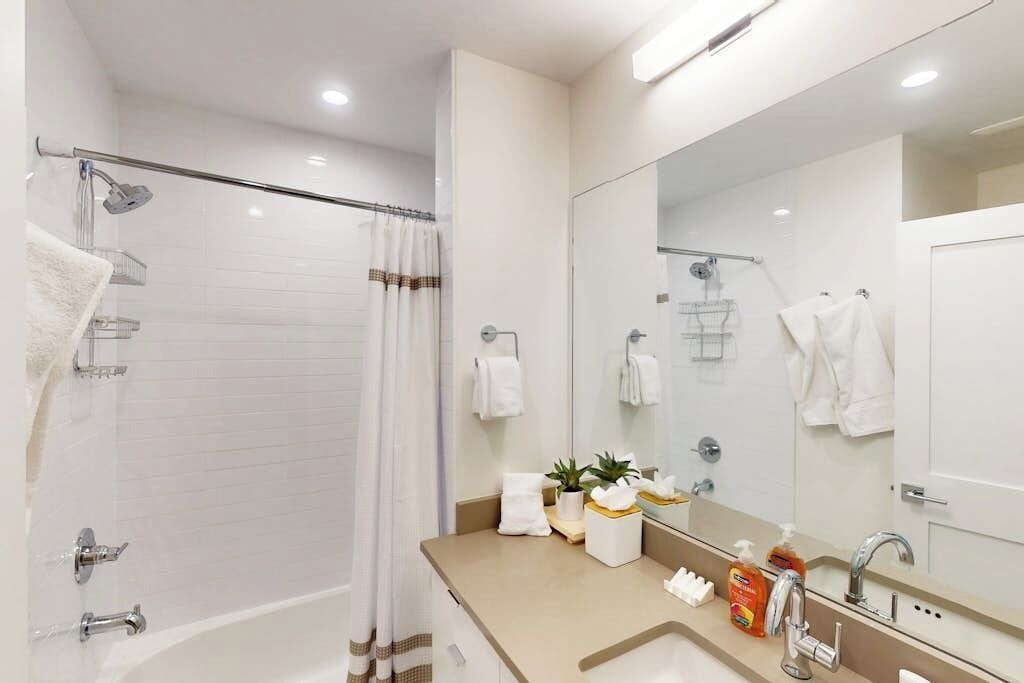 A modern bathroom with a bathtub, a shower, a large mirror, and a vanity with toiletries.