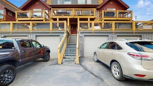 Ein mehrgeschossiges Gebäude mit einer zentralen Treppe, zwei Garagen und einem Parkplatz mit zwei Fahrzeugen.