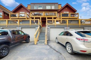 Ein mehrgeschossiges Gebäude mit einer zentralen Treppe, zwei Garagen und einem Parkplatz mit zwei Fahrzeugen.