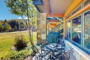 Eine Terrasse mit Gartenmöbeln, einer Stein Säule und Blick auf ein bewaldetes Gebiet.