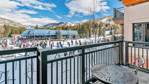 A balcony with a view of a ski resort, a covered seating area, and a mountain backdrop. - Ski-in/out condo with fireplace, balcony, fast WiFi & shared hot tub, pool, W/D (Vail)