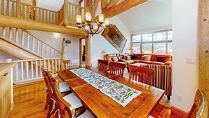 A spacious loft-style room with a wooden staircase, a dining area with a long table, and a cozy seating area with a sofa and chairs. - Enchanting mountain oasis with hot tub, fireplaces, deck, & views (Fraser)