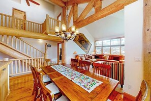 Ein geräumiger Loftsraum mit einer Holztreppe, einem Essbereich mit einem langen Tisch und einer gemütlichen Sitzecke mit Sofa und Sesseln.