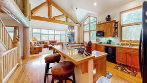 A spacious kitchen with wooden cabinets, a large island, and a dining area with a sofa and chairs. - Enchanting mountain oasis with hot tub, fireplaces, deck, & views (Fraser)