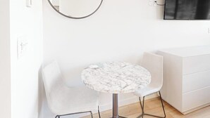 Una habitación moderna con una mesa redonda de mármol, una silla blanca, un armario blanco y un televisor de pared.