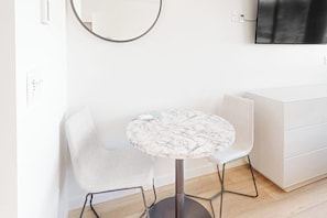 A modern room with a round marble table, a white chair, a white cabinet, and a mounted TV. - Modern ground-floor studio with mountain view, kitchenette & parking (Fraser)