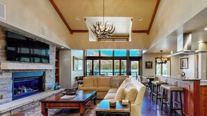 A spacious living area with a fireplace, a large sofa, a coffee table, and a kitchen area with a bar. - Ski-in/ski-out condo w/ balcony, fireplace, fast WiFi, W/D & shared pool/hot tub (Vail)