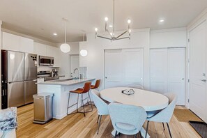 A modern kitchen with stainless steel appliances, a central island with seating, and a dining area with a round table. - Mountain-view condo with private hot tub & heated 1-car garage with EV charger (Fraser)