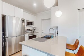A modern kitchen with stainless steel appliances, a central island with a sink, and a microwave above the oven. - Mountain-view condo with private hot tub & heated 1-car garage with EV charger (Fraser)