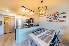 Una cocina moderna con una isla central, un área de comedor con mesa y sillas, y señalización direccional en la pared.