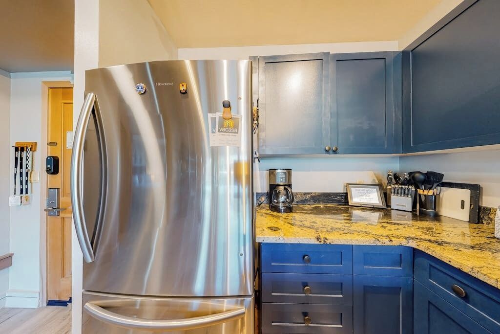 A stainless steel refrigerator, blue cabinets, a granite countertop, and a coffee maker.