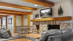 A living room with a stone fireplace, leather sofas, a wooden coffee table, and a television mounted above the fireplace.