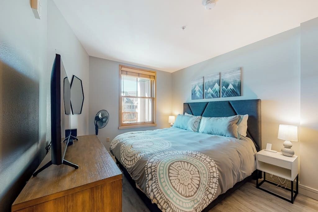Une chambre à coucher avec un lit, une table de chevet, une lampe et un téléviseur posé sur un meuble.