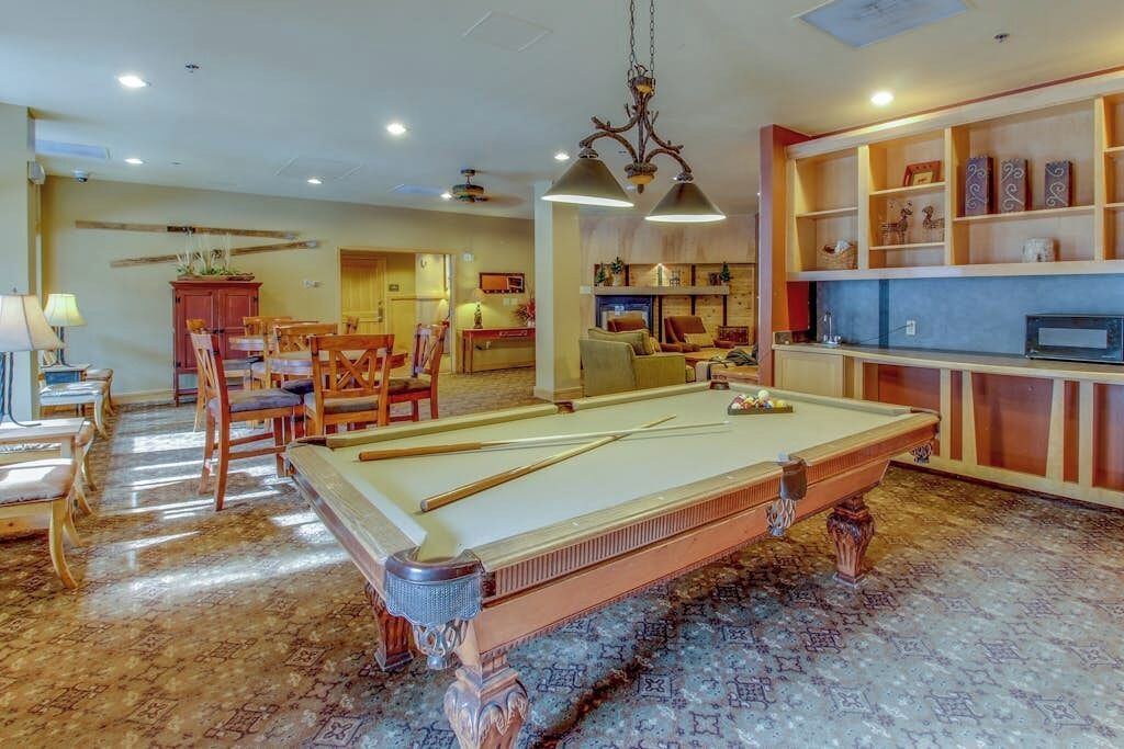 A pool table in a room with a dining area, a fireplace, and a bookshelf.