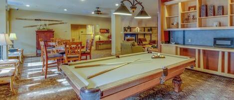 A pool table in a room with a dining area, a fireplace, and a bookshelf.