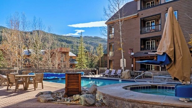 A pool area with lounge chairs and a table, a wooden building with balconies, and a mountainous backdrop.