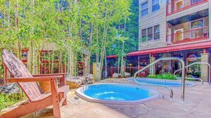 A pool area with a wooden chair, a hot tub, and a building with balconies.