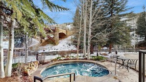 A pool area with a stone deck, a hot tub, and a stone bridge in the background. - Family-Friendly Chalet in Ski-In/Ski-Out Complex w/ Shared Pool, Hot Tubs, WiFi (Vail)