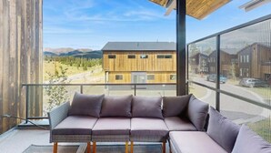 Et moderne interiør med en modulsofa, store vinduer og udsigt til en bygning og bjerge.