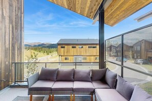 Ein modernes Interieur mit einem Ecksofa, großen Fenstern und Blick auf ein Gebäude sowie Berge.