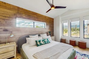 Ein Schlafzimmer mit Bett, Holzvertäfelung, Deckenventilator, Nachttisch, Fenster und Blick ins Freie.