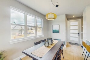A dining area with a long table, chairs, a hanging light fixture, and a large window with a view. - Inviting Condo with Mountain Views, Fireplace & Space for the Entire Family (Fraser)