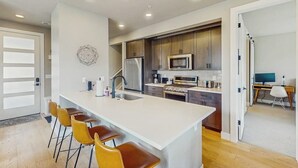 Una cocina moderna con una isla central, taburetes de bar y un comedor con una computadora y una silla.