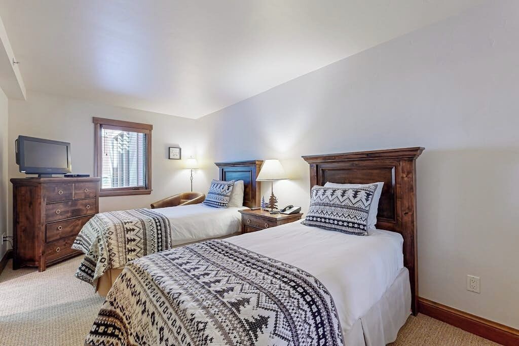 Une chambre avec deux lits, une commode, un téléviseur et une fenêtre.