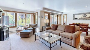 A spacious living room with a large window, a fireplace, a sofa, and a coffee table. - Chalet in Ski-In/Ski-Out Building w/ Balcony, Shared Hot Tub, Pool, W/D, WiFi (Vail)