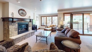 A living room with a stone fireplace, a sofa, a coffee table, and a television. - Chalet in Ski-In/Ski-Out Building w/ Balcony, Shared Hot Tub, Pool, W/D, WiFi (Vail)