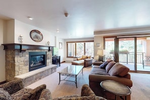 A living room with a stone fireplace, a sofa, a coffee table, and a television. - Chalet in Ski-In/Ski-Out Building w/ Balcony, Shared Hot Tub, Pool, W/D, WiFi (Vail)