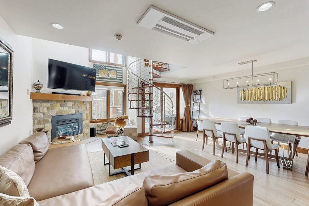 A modern living room with a fireplace, a TV, a dining area, and a spiral staircase.