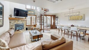 A modern living room with a fireplace, a TV, a dining area, and a spiral staircase. - Winter Condo in Ski-In/Ski-Out Complex w/gondola view, shared pool, hot tub, W/D (Vail)