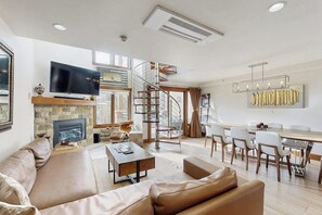 A modern living room with a fireplace, a TV, a dining area, and a spiral staircase. - Winter Condo in Ski-In/Ski-Out Complex w/gondola view, shared pool, hot tub, W/D (Vail)