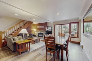 A spacious living area with a fireplace, a dining table, and a staircase leading to an upper level. - Family Home in Ski-In/Ski-Out Building w/Free WiFi & shared pool, hot tubs, W/D (Vail)