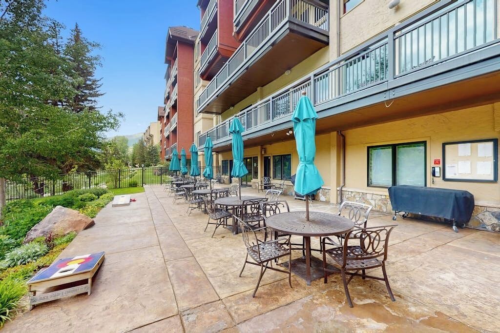 An outdoor patio with tables and chairs, a covered seating area, and a building with balconies.