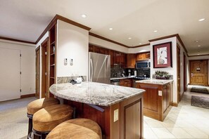 A modern kitchen with wooden cabinets, a granite countertop, and a built-in island with stools. - Mountain-view condo at ski-in/out property - outdoor pool, hot tub, walk to bus (Vail)