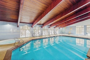 Ein Hallenbad mit Holzbalken, klaren Glaswänden und einem gefliesten Boden.