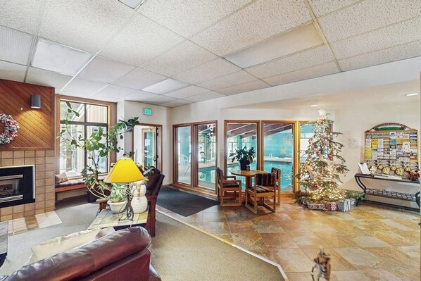 A lobby with a fireplace, seating area, Christmas tree, and a pool view. - Beaver Village condo with heated bathroom floors and free ski shuttle (Winter Park)